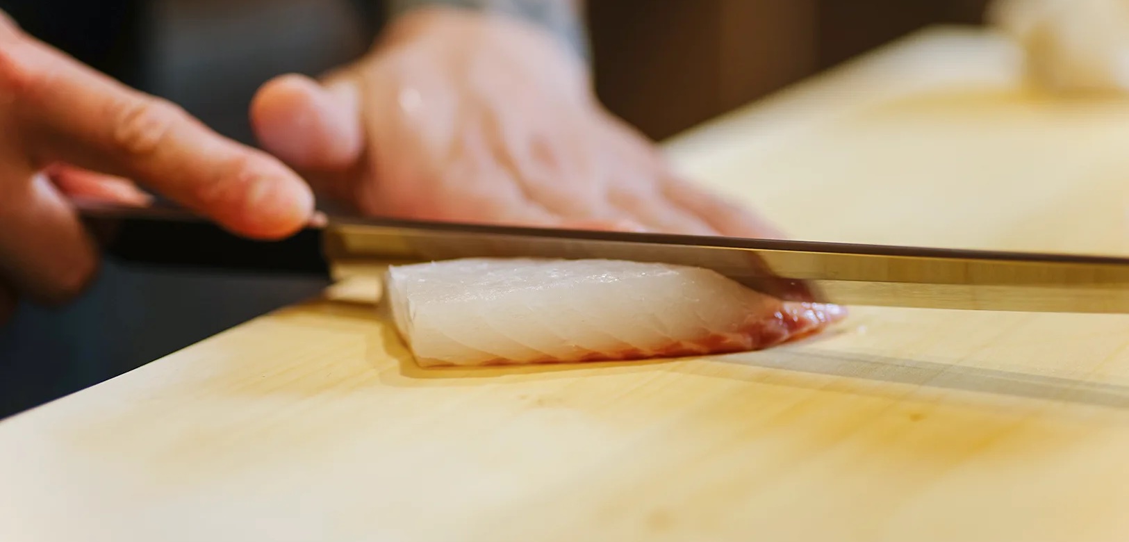 A sushi knife slicing a block of fish on a hinoki board